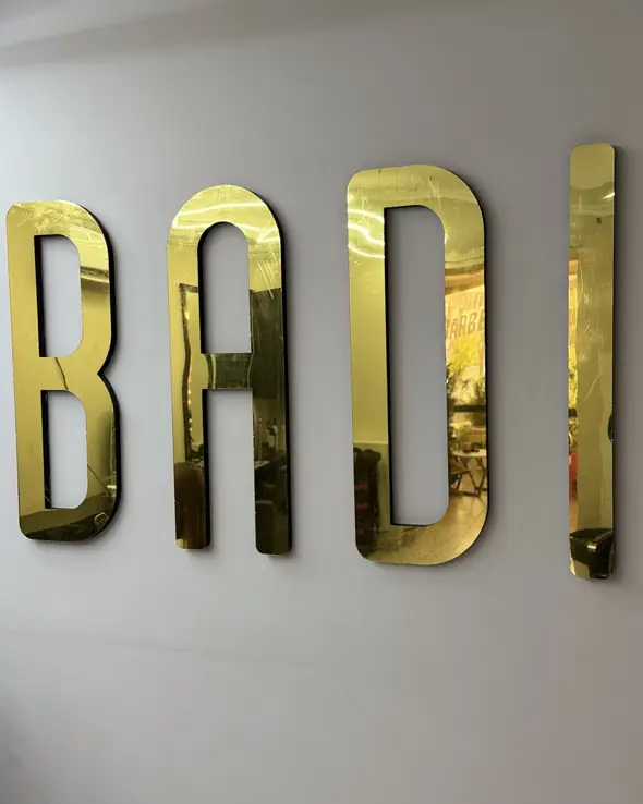 Золотые зеркальные буквы BADI на белой стене